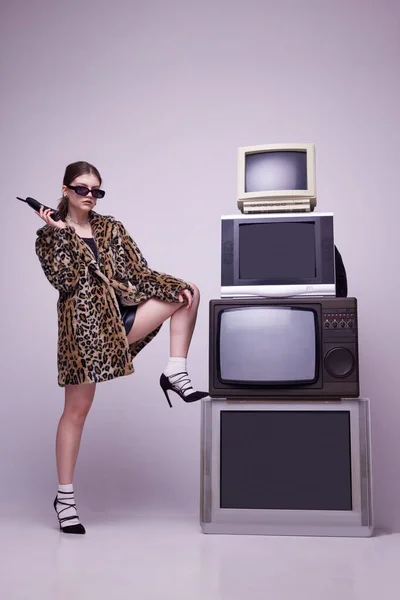 stock image Television creative manager. Young girl in stylish animal print coat and sunglasses posing near retro TV sets against grey background. Concept of fashion, 80s, 90s style, retro and vintage, mass media