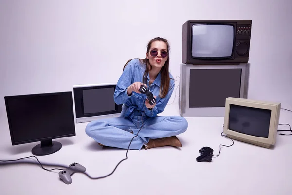 穿着牛仔裤的小女孩坐在地板上 坐在许多复古电视机旁 情绪激动地玩着游戏机 进入游戏 游戏概念 休闲活动 90年代风格 复古和复古 小玩意 — 图库照片