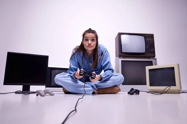 穿着牛仔裤的小女孩坐在地板上 身边有许多复古电视机和游戏机 休闲活动 游戏概念 休闲活动 90年代风格 复古和复古 小玩意 — 图库照片