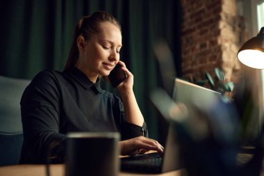 Güzel bir bayan çalışan, iş kadını masasında oturuyor, cep telefonuyla konuşuyor, dizüstü bilgisayarla çalışıyor. İş, moda, kariyer geliştirme, meslek, meslek kavramı