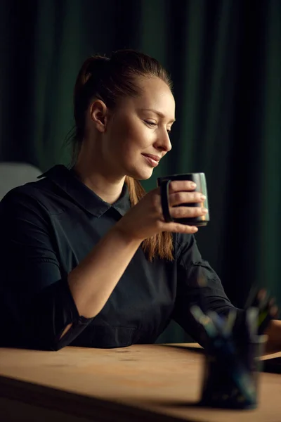 Portrait of beautiful, elegant business woman sitting at table, looking away and drinking coffee. Confidence and professionalism. Concept of business, , career development, profession, occupation