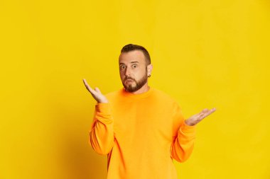 Renkli kazaklı sakallı bir adamın portresi. Şok olmuş, şaşırmış bir yüzle canlı sarı arka plana poz veriyor. İnsan duyguları kavramı, yaşam tarzı, yüz ifadesi, satış, haber. Ad