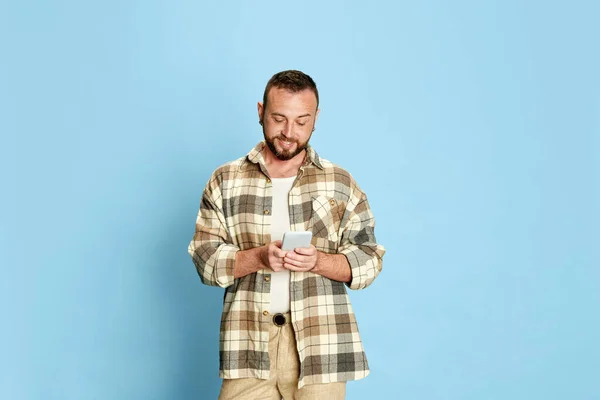 青いスタジオの背景に携帯電話でメッセージを入力チェックシャツの幸せな 髭の男の肖像画 人間の感情 ライフスタイル 表情の概念 — ストック写真