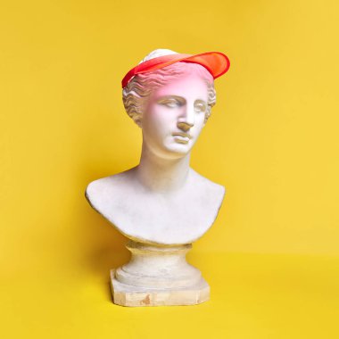 Sarı arka planda şık bir şapka takan antik bir heykel büstü. Sportif görünüş, hobi, aktif yaşam tarzı. Yaratıcılık kavramı, modernlik ve bağbozumu, antik sanat. İlham ve hayal gücü