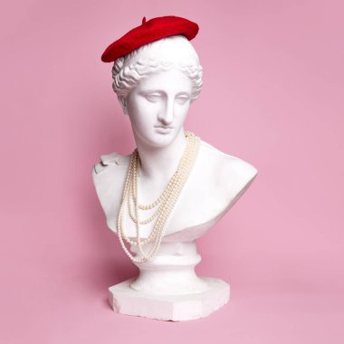 Pembe arka planda kırmızı bereli ve inci kolyeli güzel bir kadının antik heykel büstü. Parisli gibi görünüyorsun. Yaratıcılık kavramı, modernlik ve bağbozumu, antik sanat. İlham ve hayal gücü