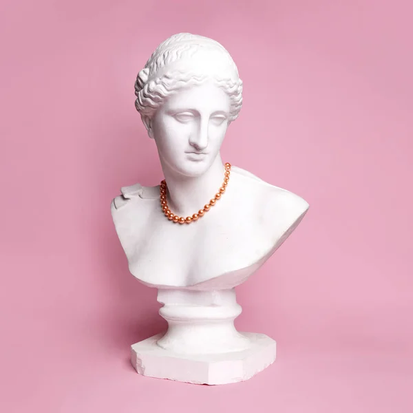 Antique statue bust of pretty woman in red beautiful necklace against pink background. Femininity. Concept of creativity, modernity and vintage, antique art. Inspiration and imagination