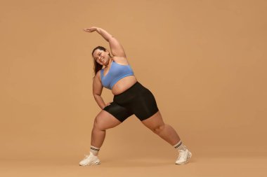 Esniyorum. Kahverengi stüdyo geçmişine karşı spor giyimi eğitimi alan şişman bir kadın. Antrenman yapmak için motivasyon. Spor anlayışı, vücut pozitifliği, kilo kaybı, vücut ve sağlık hizmetleri