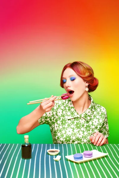 お箸でグラデーションの虹を背景に甘いマカロンを食べる お洒落で若い女の子 醤油味 フードポップアート写真 レトロなスタイル 創造的なビジョン 想像力の概念 — ストック写真