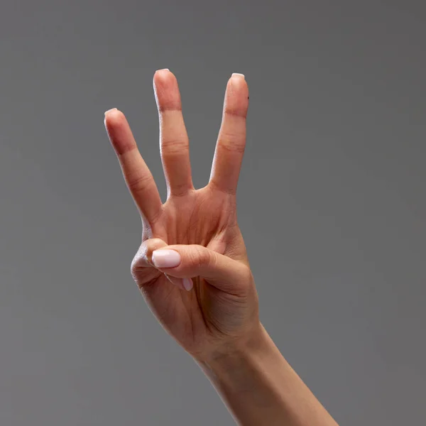 Female hand showing gesture with three fingers against grey background. Concept of human relation, community, symbolism, culture, communication, signals