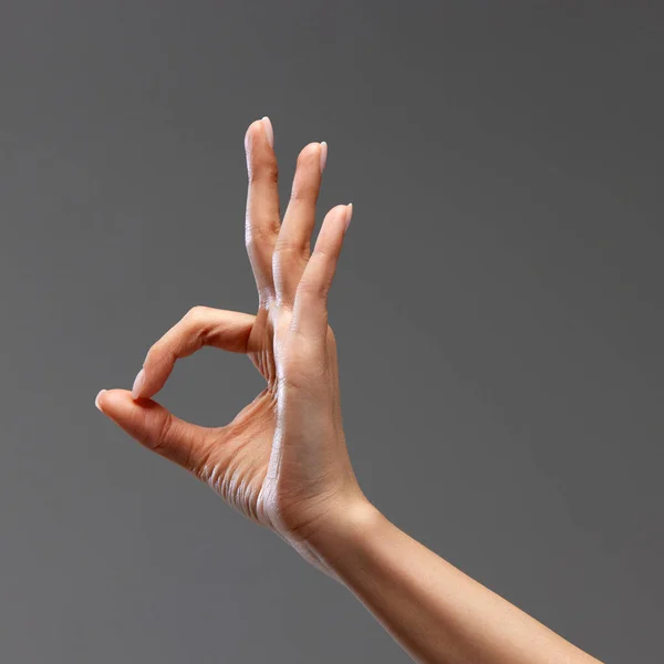 Female hand showing gesture of OK against grey background. Good time, approvement signals, acceptance. Concept of human relation, community, symbolism, culture, cummunication