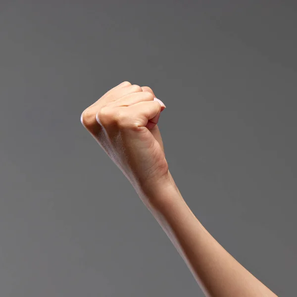 Female hand showing fist against grey background. Freedom of speech, equality, fighting against wrong situations. Concept of human relation, community, symbolism, culture, communication