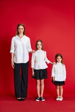 Güzel bir genç kadın ve iki küçük kızın portresi. Kırmızı stüdyo arka planında poz veren anne ve kızları. Destek. Aile kavramı, annelik, çocukluk, moda, yaşam tarzı