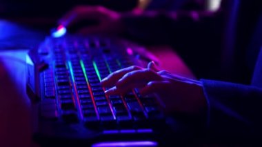 Erkek ellerinin ışıklarla hızlı bir şekilde bilgisayar klavyesine basarak çevrimiçi oyunlar oynamak için bilgisayar faresini kullanması. Neon ışığı. Siber spor kavramı, online video oyunları, modern teknolojiler.