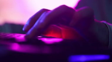 Erkek ellerine yakın çekim, sanal sporcu çevrimiçi oyunlar oynamak için arka planda klavye kullanıyor. Neon ışıklandırılmış arka plan. Siber spor kavramı, online oyun, modern teknolojiler, serbest çalışma