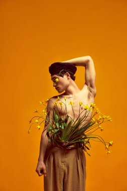 Çiçek açma stili. Çekici genç erkek portresi, siyah bereli ve bej renkli klasik pantolonlu model sarı stüdyo arka planında. Erkek modası, tarzı, sanatı, güzelliği, eğilimleri