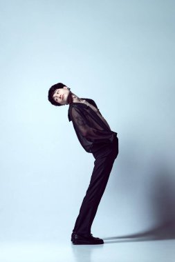 Açık mavi stüdyo arka planına karşı şeffaf siyah gömlekle poz veren yakışıklı, şık, genç bir adamın tam boy portresi. Erkekler moda, tarz, sanat, güzellik, trendler, ilham