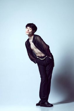 Açık mavi stüdyo arka planına karşı şeffaf siyah gömlekle poz veren yakışıklı, şık, genç bir adamın tam boy portresi. Erkekler moda, tarz, sanat, güzellik, trendler, ilham