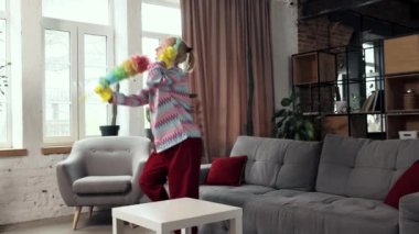 Renkli ev kıyafetleri içinde aktif genç bir kadın, temizlik yapıyor, kulaklıkla müzik dinliyor ve oturma odasında dans ediyor. Ev işleri kavramı, eğlence, duygular, boş zaman