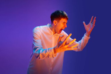 Genç duygusal bir adamın portresi, neon ışıkta belirgin bir şekilde bağırıyor, gradyan mor arka planda çığlık atıyor. Öfke, sıkıntı. İnsan duyguları, yaşam tarzı, gençlik kavramı