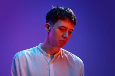 Beyaz gömlekli genç adamın portresi, neon ışıkta mor arkaplanda hüzünlü bir yüz ifadesi ile poz veriyor. Depresif bir bakış. İnsan duyguları, yaşam tarzı, gençlik kavramı