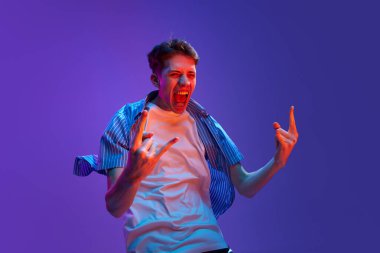 Portrait of young emotive man guy in casual clothes showing success and winning look against gradient purple background in neon light. Wind blowing effect. Concept of human emotions, lifestyle, youth clipart
