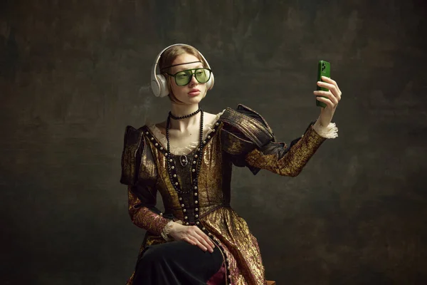 穿着老式服装 时髦太阳镜和耳机的年轻漂亮姑娘的画像 带着手机和深绿色背景 历史的概念 复兴艺术 时代的比较 — 图库照片