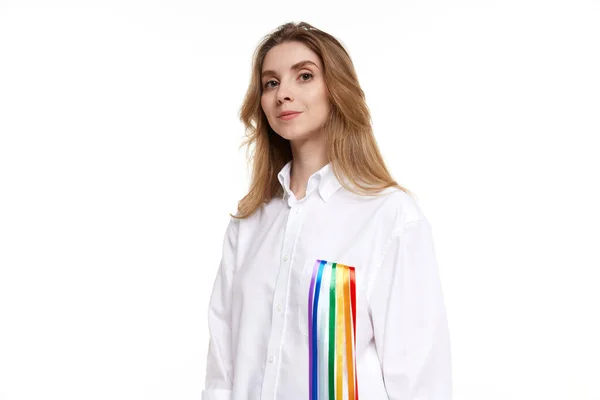 stock image Portrait of young smiling woman wearing white shirt with rainbow line symbolizing lgbt tolerance. Model posing on white background. Concept of lgbt community, support, love, human rights, pride month