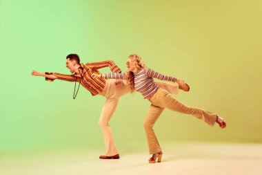 Tarz sahibi, anlamlı, yetenekli, klasik giysiler içinde yeşil arka planda dans eden genç erkek ve kadın. Eski tarz, disko dansı, moda, sanat, hobi, müzik, 70 'ler
