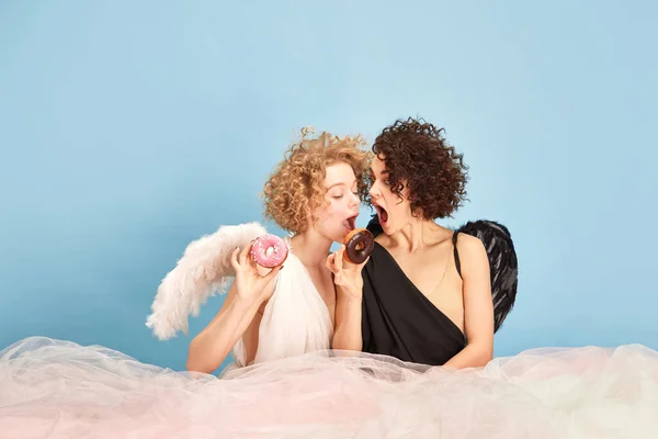 穿着天使和魔鬼服装的漂亮女人的画像 戴着蓝色红色背景的甜甜圈 甜蜜的情人 情感的概念 存在的比较 创造力 — 图库照片