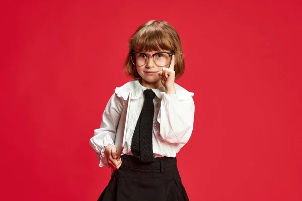 アイデアだ スマートでかわいい女の子の肖像画 白いブラウスの子供 黒いスカートと赤いスタジオの背景に指を上げる大きなメガネ 子供時代教育ファッション子供時代の感情学校のコンセプト — ストック写真