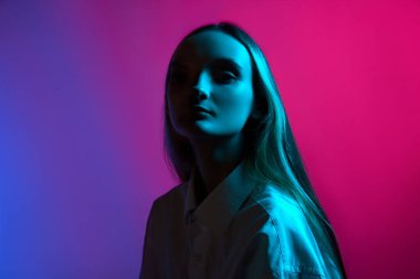 Poz veren genç bir kızın portresi, kameraya kamera ile bakıyor, neon ışıkta pembe arkaplan rengine karşı. Sanat anlayışı, modern tarz, siber punk, fütürizm ve yaratıcılık