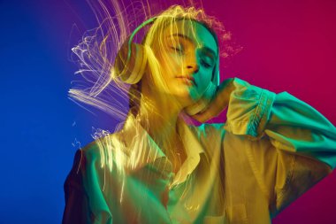 Kulaklıkla müzik dinleyen genç bir kızın portresi, karışık neon ışık efektiyle gradyan mavi arka planda poz veriyor. Sanat anlayışı, modern tarz, siber punk, fütürizm ve yaratıcılık
