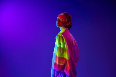Vücudunda çok renkli neon filtre yansıması olan genç bir kızın portresi, poz veriyor, mor arka planda kameraya bakıyor. Sanat kavramı, modern tarz, siber punk, gelecekçilik ve yaratıcılık, duygular.