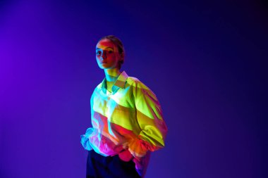 Vücudunda çok renkli neon filtre yansıması olan genç bir kızın portresi, poz veriyor, mor arka planda kameraya bakıyor. Sanat anlayışı, modern tarz, siber punk, fütürizm ve yaratıcılık