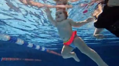 Güzel, küçük bir kız bebek, annesi kucağında yüzme havuzunda yüzen bir bebek. Su sporları aktivitesi. Spor, sağlıklı ve aktif yaşam tarzı, çocukluk, eğlence ve eğitim kavramı