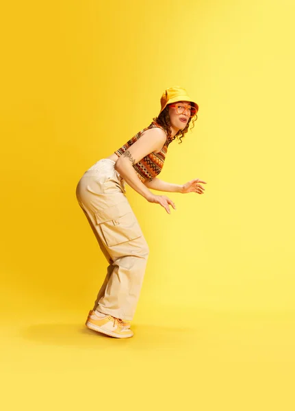 全长肖像画滑稽的年轻女孩在巴拿马 裤子和上衣与滑稽的脸与黄色工作室背景 人类情感 青年文化 生活方式 迷因的概念 — 图库照片