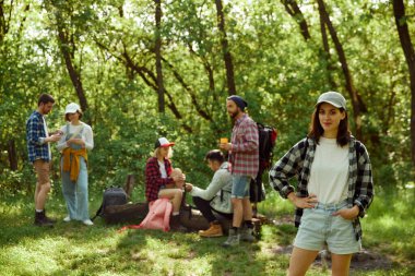 Kareli tişörtlü güzel, gülümseyen kız arkadaşlarıyla yürüyüşe çıkıyor. Bir grup genç insan sıcak bir günde ormanda piknik yapıyor. Aktif yaşam tarzı, doğa, spor ve hobi, arkadaşlık kavramı