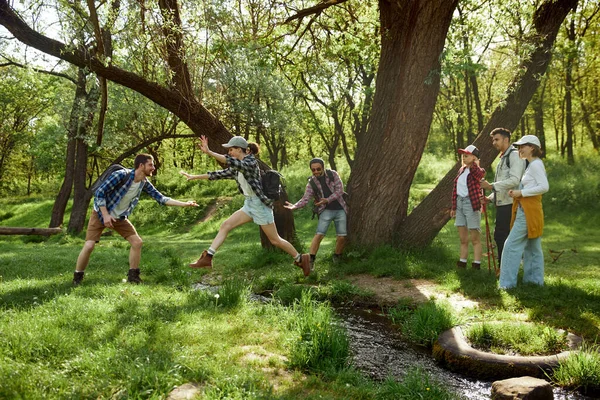年轻人 男人和女人 朋友去远足 在森林里散步 在温暖的日子里跳过河 在外面玩的开心积极生活方式 运动和业余爱好 友谊的概念 — 图库照片