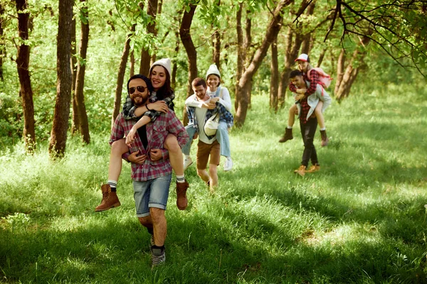 若者のグループは 友人の森の中を歩くと 暖かい晴れた日にハイキングに行く 女の子は男の子の背中に座っている アクティブなライフスタイル スポーツと趣味 レジャーと楽しみの概念 — ストック写真