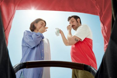 Genç ebeveynler, erkek ve kadın sıcak güneşli bir günde yürüyüş sırasında bebek arabasını inceliyor, bebek bezi tutuyor ve burnunu kapatıyorlar. Çok kötü kokuyor. Ebeveynlik kavramı, aile, duygular, bakım, mutluluk