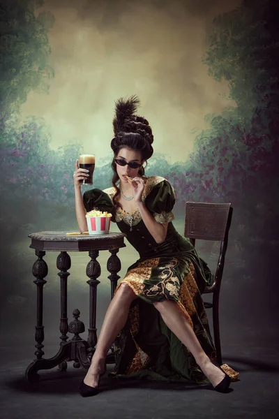 年轻女子的画像 中世纪的皇室成员 穿着雅致的衣服 坐着一大杯发泡的啤酒 在深色的老式背景下吃薯条 历史的概念 复兴艺术 时代的比较 — 图库照片