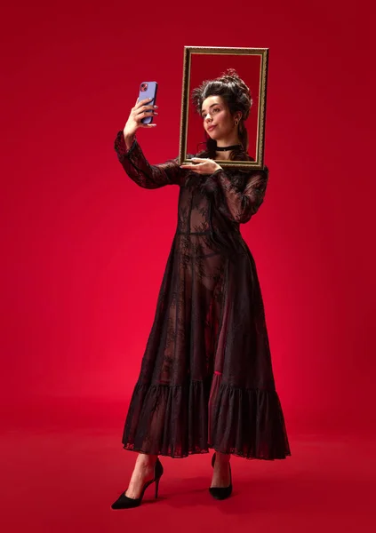 全长的画像 年轻的女孩拿着相框 拿着红色背景的手机自拍 历史的概念 复兴艺术 时代的比较 — 图库照片