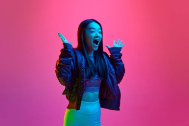 Neon ışıkta pembe stüdyo arka planına karşı pozitif şok ifadesiyle poz veren Koreli genç bir kızın portresi. - Sürpriz. Duyguların kavramı, yüz ifadesi, gençlik, yaşam tarzı, ilham, reklam