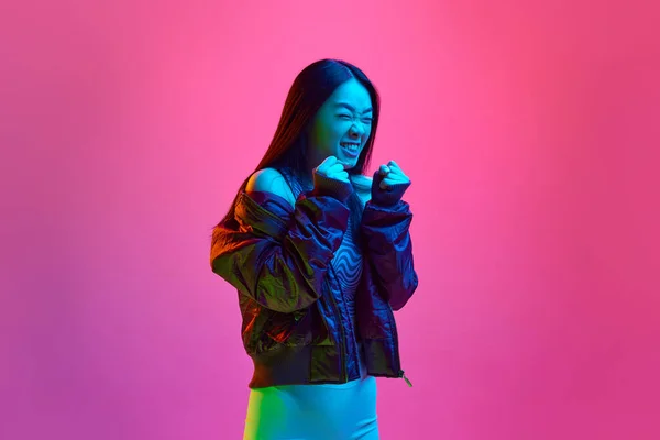 穿着休闲装的年轻韩国女孩在霓虹灯下 在粉红的工作室背景下摆出拳头的肖像 情感概念 面部表情 生活方式 — 图库照片