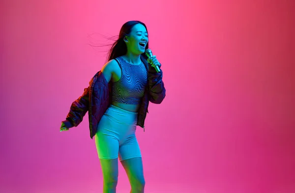 在霓虹灯下的粉红录音棚背景下 年轻女孩在麦克风中歌唱的快乐 微笑的画像 卡拉Ok的乐趣 情感概念 面部表情 生活方式 — 图库照片