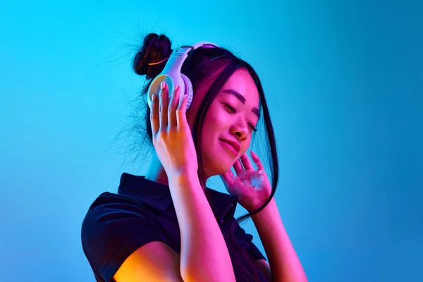 ネオンの青スタジオを背景にヘッドフォンで音楽を聴く美しい韓国の少女の肖像画 感情の概念 顔の表情 ライフスタイル インスピレーション — ストック写真