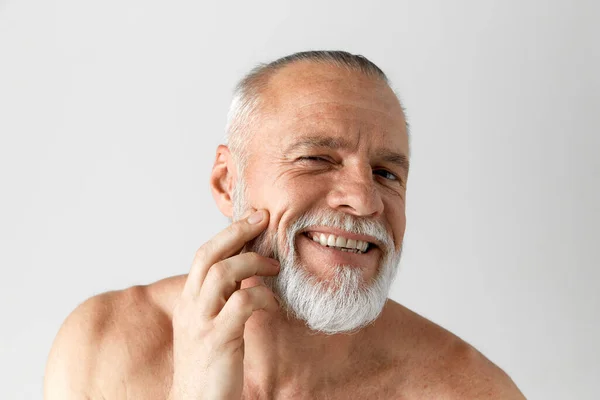 アンチエイジングケア 白髪のハンサムな髭を生やした男の肖像画 灰色の背景に笑顔で肌をよく保ちます 男性の美しさ 顔と肌のケア 毎日の手順 年齢の概念 — ストック写真