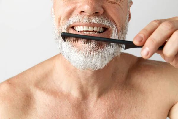 ひげの後の世話をする灰色の髪を持つハンサムな成熟した男の肖像画 それをブラッシング 灰色の背景に対して軽率なポーズ 男性の美しさ 顔と肌のケア 毎日の手順 年齢の概念 — ストック写真