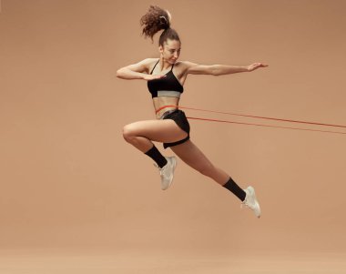 Sportif, formda, hareketli genç kız eğitiminin dinamik görüntüsü açık kahverengi stüdyo arka planına zıplıyor. Spor yaşam tarzı, güzellik, vücut bakımı, fitness, sağlık konsepti