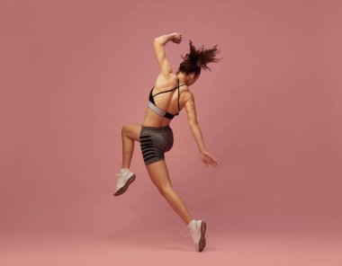 Tüm vücut egzersizi. Spor giyinen genç bir kadının dinamik görüntüsü. Pembe stüdyo geçmişine karşı hareket halinde. Spor yaşam tarzı, güzellik, vücut bakımı, fitness, sağlık
